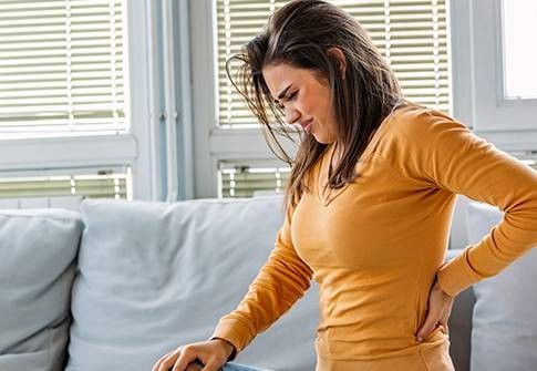 donna seduta su un divano che si tocca la schiena