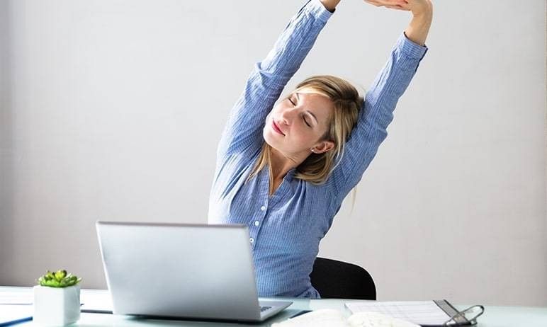 donna in postazione di ufficio che allunga la schiena